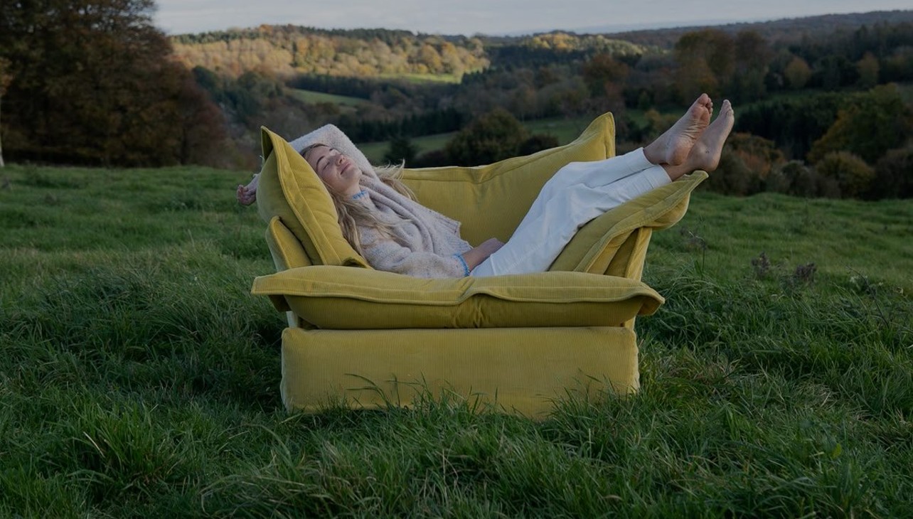 Mulher descansando em um sofá amarelo em meio a um campo verde